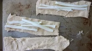Roll out and cut the dough into thin strips. Lay out the cheese.