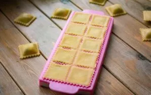 Cover with a second thin layer of dough and roll with a rolling pin several times with force so that the edges of future ravioli appear.