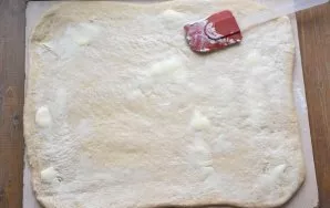 Sprinkle the work surface with flour and roll out the dough into a rectangular shape with a rolling pin. Grease the surface with soft but...