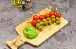 Peel the avocado and cut into slices, sprinkle with lemon juice. Roll cherry tomatoes and olives on skewers.