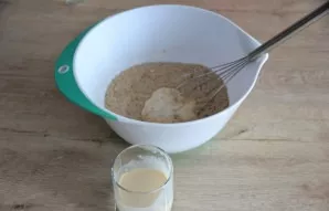 Pour ryazhenka (or kefir) in portions and add to the dough.