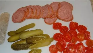 Take the smoked sausage and cut it into pieces. We also chop the cucumber and tomatoes. Try to make the slices thinner.