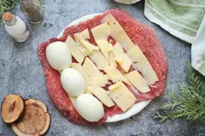 Cut the cheese into thin strips and spread over the entire surface of the pork. Peel the eggs and cut them in half. Place them in one row...