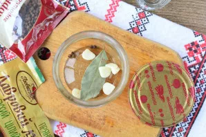 Add spices to the bottom of a 0.5 liter jar: pepper peas, bay leaf and pieces of peeled garlic.