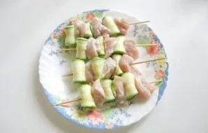On wooden skewers alternately put pieces of chicken fillet and zucchini plates that need to be twisted.