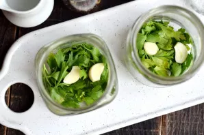 Wash the greens in hot water, put on the bottom of the jars. Peel the garlic, cut the cloves into two parts, put in jars.
