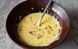 Add ground black pepper to the mixture of parmesan and eggs in a bowl and mix everything with a fork until smooth.