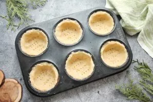 Divide the dough into equal parts and distribute it into molds in a thin layer. Beat the bottom with a fork.