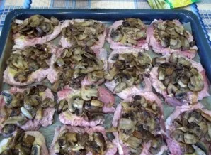 Now we cover the baking sheet with baking paper and put the beaten meat, sprinkle with salt and pepper, and put mushrooms and onions on top.