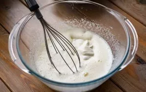 Pour vegetable oil into the egg mixture and add sour cream. Stir everything with a whisk.
